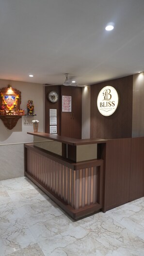 Un mostrador de recepción de hotel con detalles de madera, un reloj y un cartel con los horarios de salida.