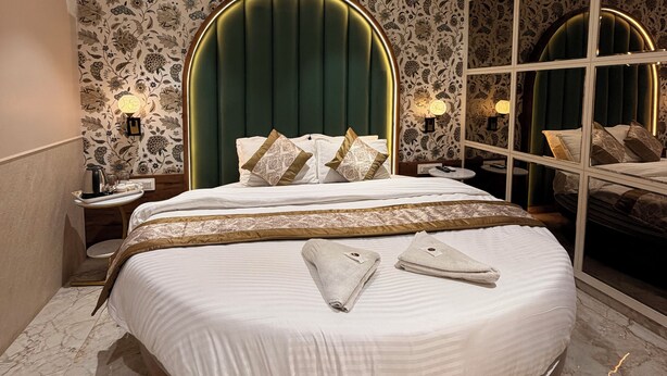Um quarto moderno com uma cama redonda, cabeceira estofada em verde e papel de parede estampado.