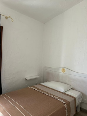 A bedroom with a bed, a bedside table, and a wall-mounted shelf.