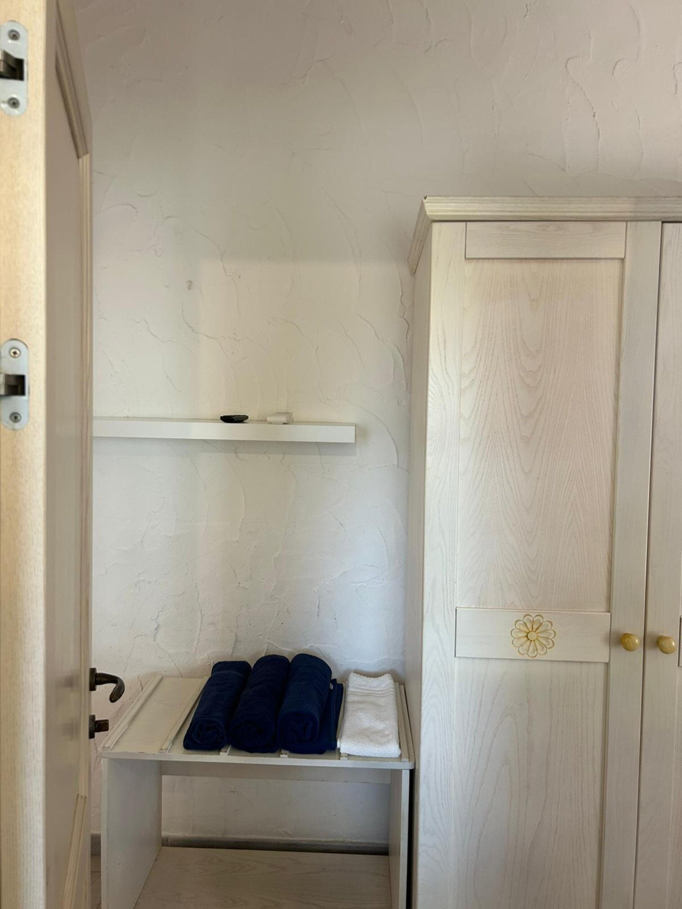 A small room with a white wardrobe, a shelf with folded towels, and a door with a handle.