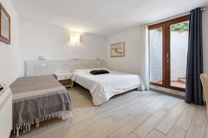 A bedroom with two beds, a nightstand, a wall-mounted light, a painting, and a sliding glass door to the outside.