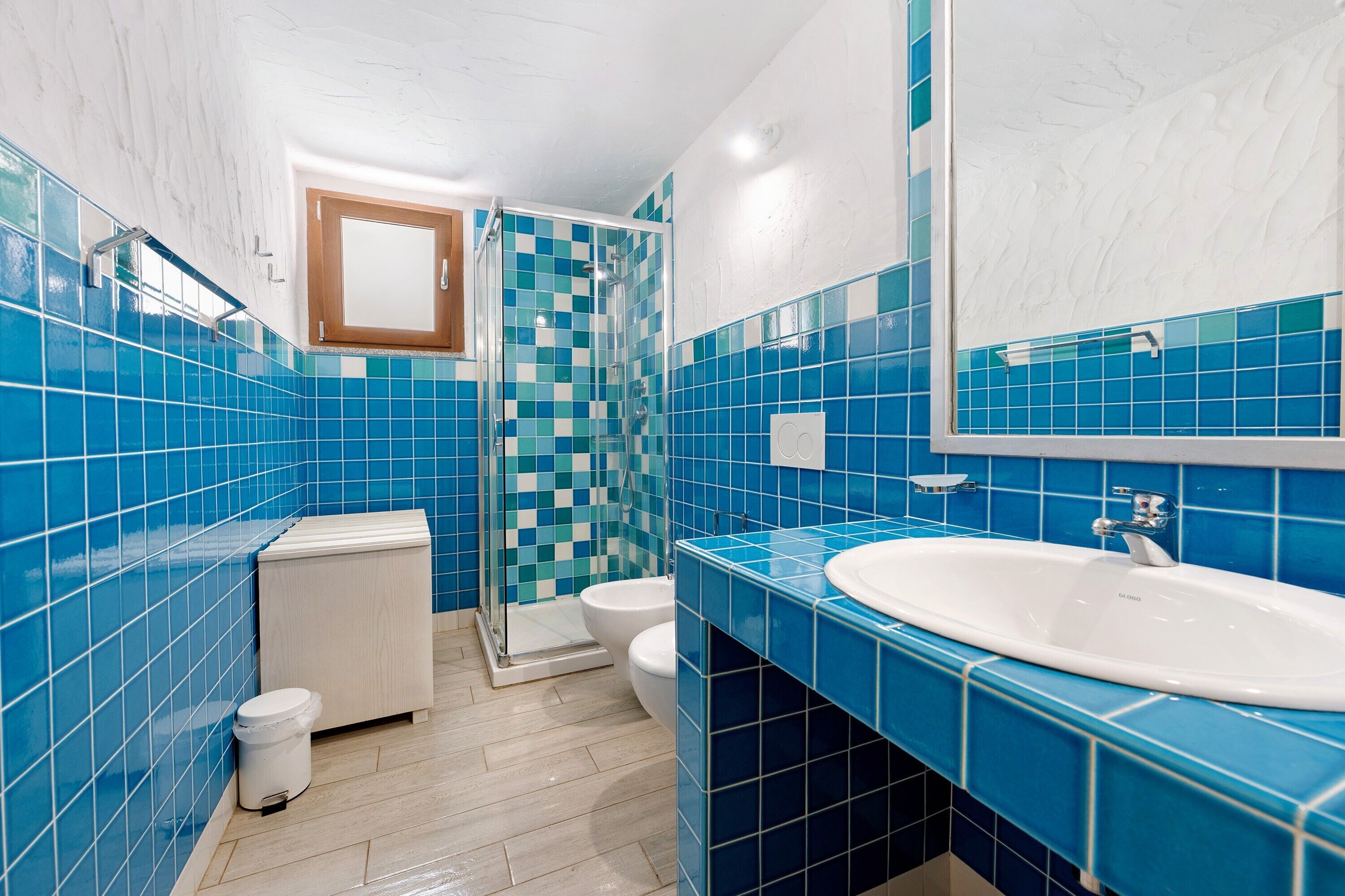 A bathroom with blue tiles, a white sink, a mirror, a shower, and a toilet.