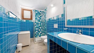 A bathroom with blue tiles, a white sink, a mirror, a shower, and a toilet.