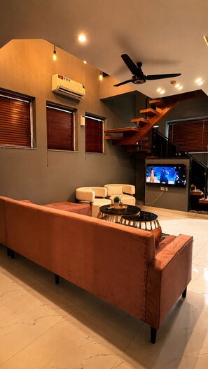 A modern living room with a sofa, a ceiling fan, recessed lighting, and a staircase.