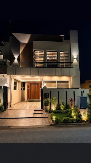 A modern two-story house with a front entrance, a balcony, and a well-lit driveway. - Spacious 3BR Home in DHA Rahbar - WiFi, Parking & 24/7 Support (Lahore)