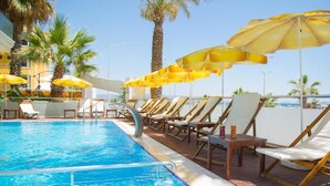 A swimming pool with sun loungers and umbrellas, surrounded by palm trees and a clear sky. - Acem Hotel (Ayvalik)