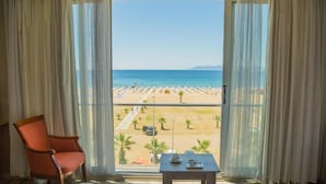 A hotel room with a large window, a bed, a chair, and a small table with a cup and saucer. - Acem Hotel (Ayvalik)