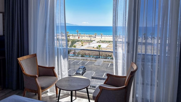 A hotel room with a balcony, two chairs, a small table, and a view of the beach and ocean. - Acem Hotel (Ayvalik)