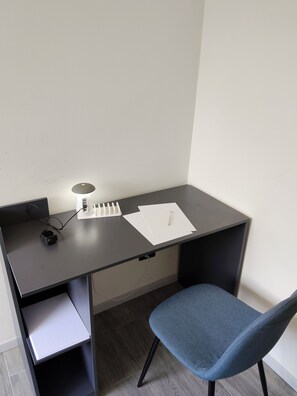 A small, dark-colored desk with a lamp, papers, and a pen. There is a chair with a blue cushion. - Spacious Apartment in a Convenient Location (Bergamo)