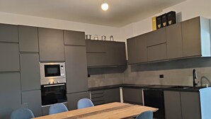 Moderni keittiö, jossa on harmaat kaapit, puinen ruokapöytä ja siniset tuolit.