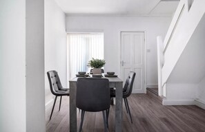 A dining area with a table, four chairs, a potted plant, and a staircase.
