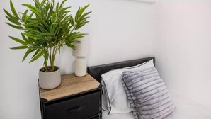 Un dormitorio con una cama, una mesita de noche con una lámpara y una planta en maceta.