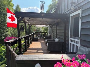 A covered outdoor deck with a Canadian flag, outdoor furniture, and a garden area.