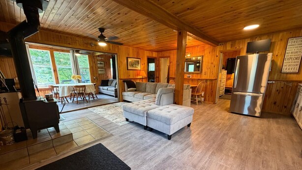 Interior de uma cabana de madeira com sala de estar, área de refeições, cozinha e uma janela grande.