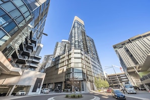 A modern high-rise building with a curved facade, multiple balconies, and a parking area with cars.
