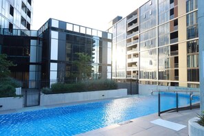 A modern building with a swimming pool, surrounded by greenery and a metal fence. - Heart of Belconnen/2BR/2BA/pool/spa/sauna/gym/UC (Belconnen)