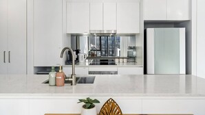 Cozinha moderna com armários brancos, eletrodomésticos de aço inoxidável e uma ilha central com pia e bancada.