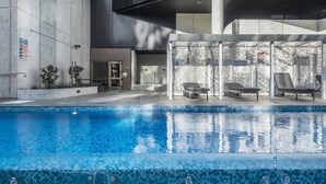 Uma área de piscina moderna com piscina transparente, espreguiçadeiras e um espaço de estar coberto.