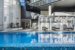 A modern pool area with a clear pool, lounge chairs, and a covered seating area.