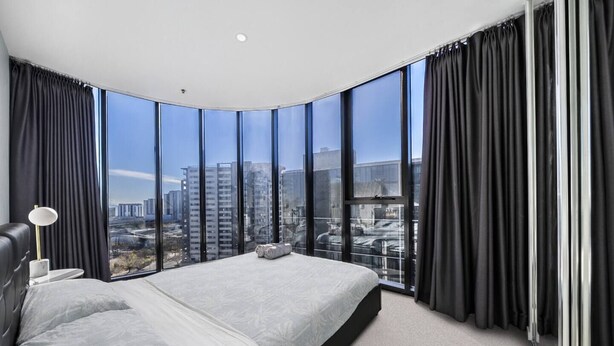Quarto moderno com teto arredondado, janelas amplas, cama e mesa de cabeceira.