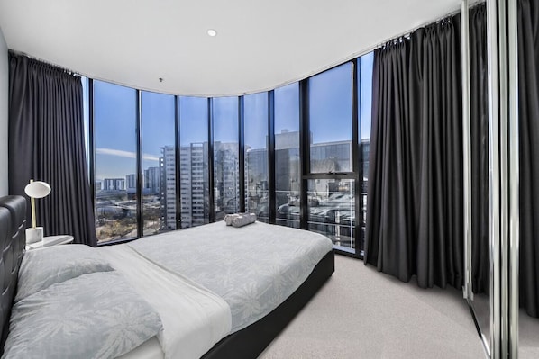 A modern bedroom with a curved ceiling, large windows, a bed, and a nightstand.