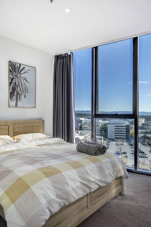 A bedroom with a large window, a bed, a headboard, and a painting on the wall. - Heart of Belconnen/2BR/2BA/pool/spa/sauna/gym/UC (Belconnen)
