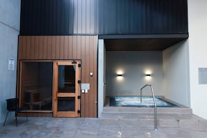 A spa entrance with a wooden door, a hot tub, and a chair outside.