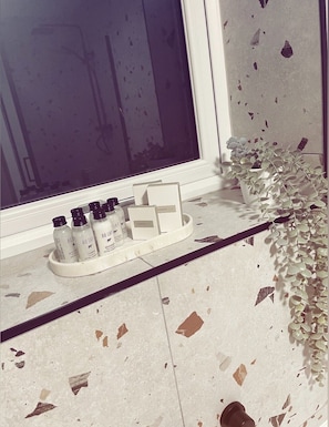 A bathroom vanity with a window, a potted plant, and a tray with toiletry bottles and a sewing kit.