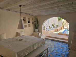 Un dormitorio con cama, mesita de noche, lámpara y vistas a una piscina exterior a través de un arco.