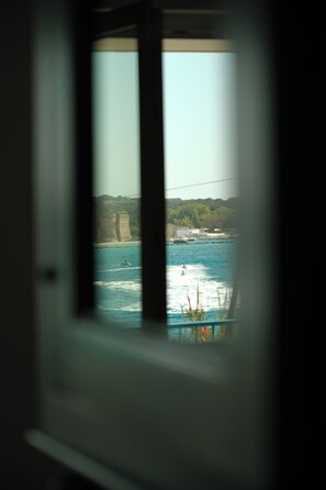 Blick durch ein Fenster auf eine Küstenlandschaft mit Klippen, einer Wasserfläche und einer fernen Uferlinie.