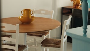 A dining area with a round wooden table, white chairs with woven seats, and a yellow pitcher on the table. - Casa Totò - Ocean View in the Center of Otranto Terrarossa Luxury Home (Otranto)