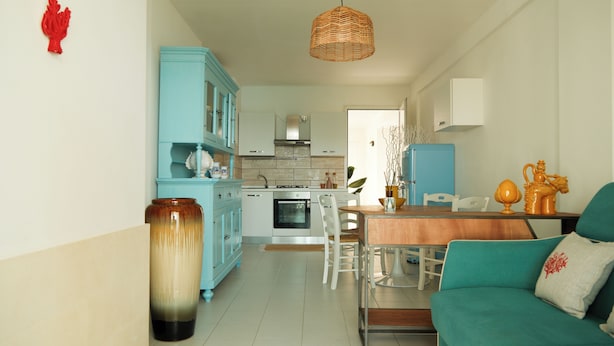 A modern kitchen with a dining area, a teal sofa, and a wicker pendant light. - Casa Totò - Ocean View in the Center of Otranto Terrarossa Luxury Home (Otranto)