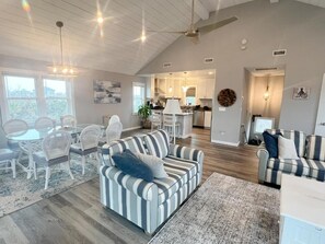A spacious living area with a high ceiling, a dining table with chairs, a striped sofa, and a kitchen in the background. - Kate's Catch- 500 Ft To The Beach! (Hatteras)