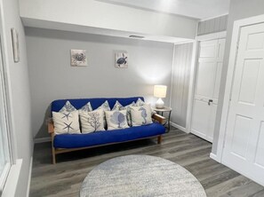 Ett rum med en blå soffa, en rund matta, en lampa och två konstverk på väggen.