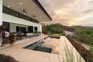 Ein modernes Haus mit Pool, Sitzgelegenheiten im Freien und Blick auf die umliegende Landschaft.