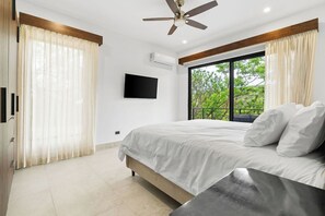 A bedroom with a bed, a ceiling fan, a TV, and a window with curtains. - Casa Alto Verde | 4 King Suites & Pool (Playas del Coco)