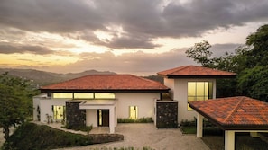 A modern two-story house with a red-tiled roof, large windows, and a landscaped garden. - Casa Alto Verde | 4 King Suites & Pool (Playas del Coco)