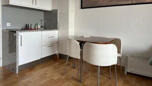 Una cocina moderna con gabinetes blancos, encimera de granito y comedor con mesa y sillas blancas.