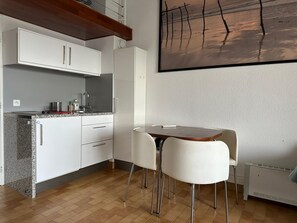 Eine moderne Küche mit weißen Schränken, einer Arbeitsplatte aus Granit und einem Essbereich mit weißem Tisch und Stühlen.