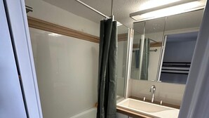 Un baño pequeño con ducha, lavabo y espejo.