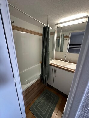 Ein kleines Badezimmer mit Dusche, Waschbecken und Spiegel.