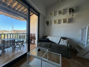 Ein Balkon mit Blick auf das Meer und Gebäude, eine Sitzecke mit Sofa, ein Glastisch und eine Treppe.