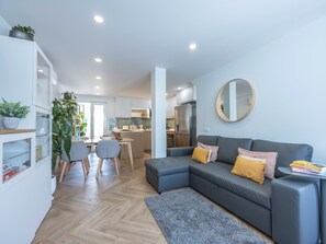 Eine moderne Wohnung mit grauem Sofa, einem Esstisch und einer Küche im Hintergrund.