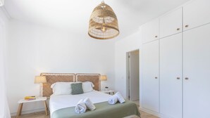 A bedroom with a bed, bedside tables, a hanging light fixture, a wardrobe, and a door. - Alvor Arcos Beach - sun, pool and village calm (Montenegro)