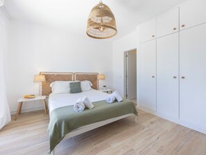 Ein Schlafzimmer mit einem Bett, Nachttischen, einer Hängeleuchte, einem Kleiderschrank und einer Tür.