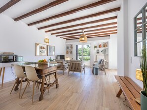 Eine geräumige Küche mit Holzbalken, ein Essbereich mit Holztisch und -stühlen sowie ein Blick ins Freie durch eine Glastür.