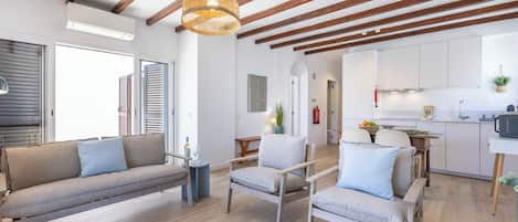 A modern living room with a sofa, chairs, a hanging light fixture, and a kitchen area with cabinets and a sink.
