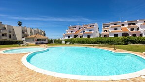 A swimming pool with a tiled deck, surrounded by white buildings with orange roofs, and a clear blue sky. - Alvor Arcos Beach - sun, pool and village calm (Montenegro)