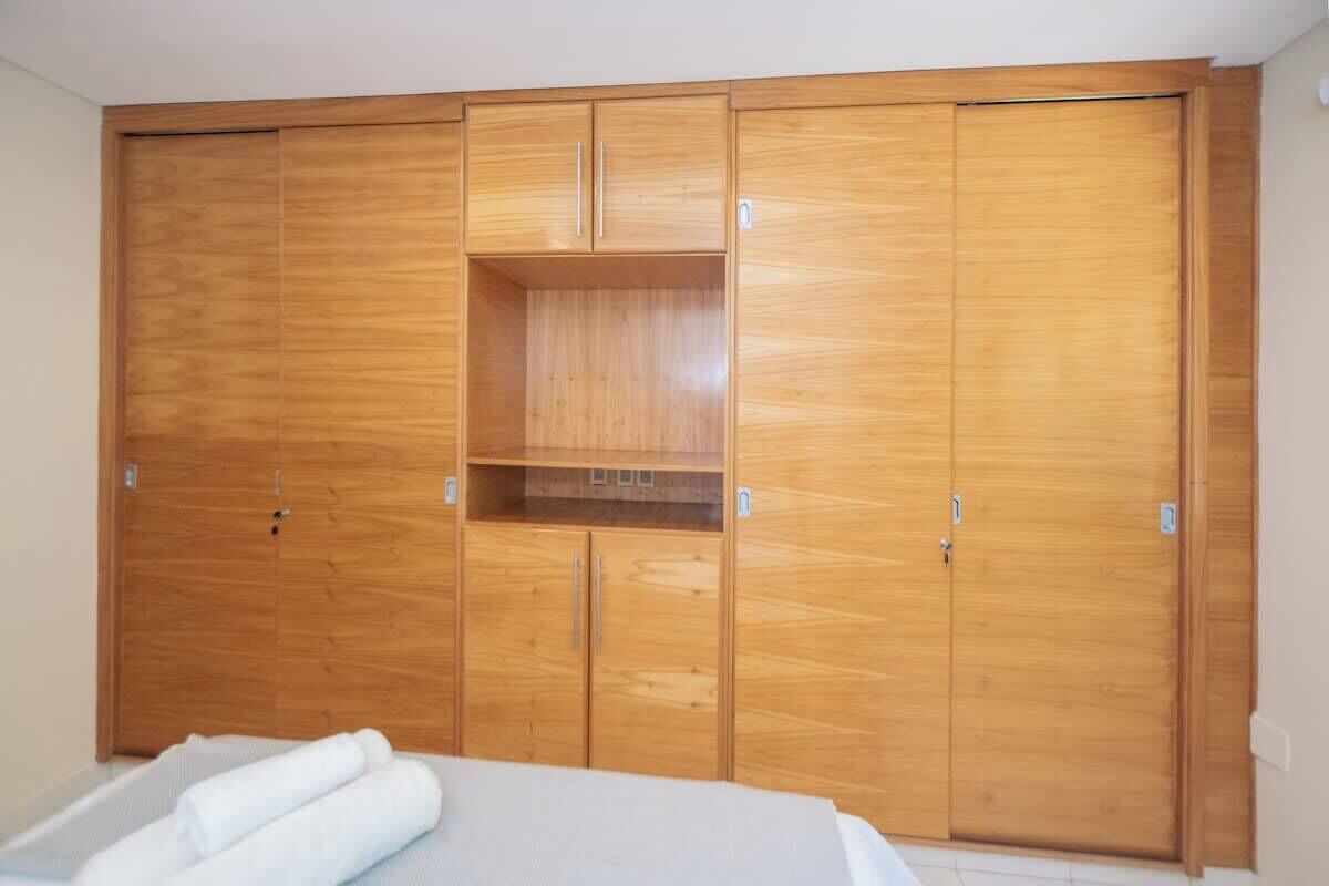 Een slaapkamer met een houten garderobe, een bed en een klein wandrek.