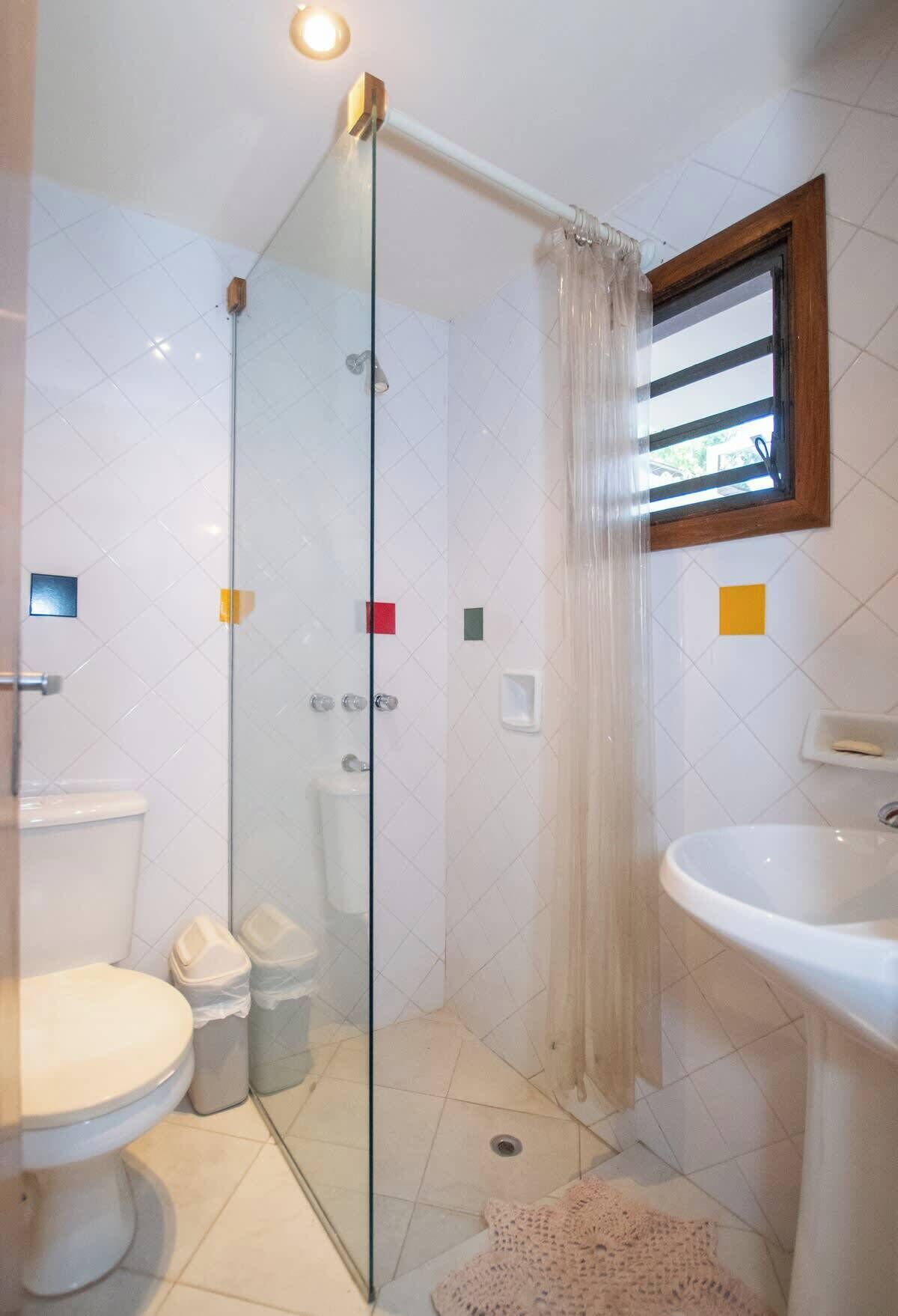 A bathroom with a glass shower enclosure, a toilet, a sink, and a window with a curtain.